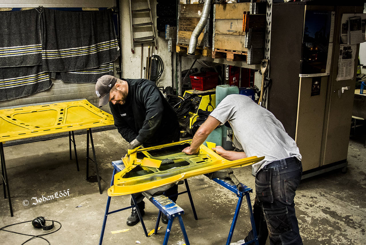 Two men work on a car door in a garage